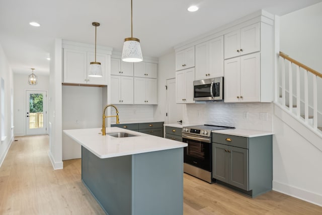 kitchen with sink, appliances with stainless steel finishes, decorative light fixtures, an island with sink, and light hardwood / wood-style flooring