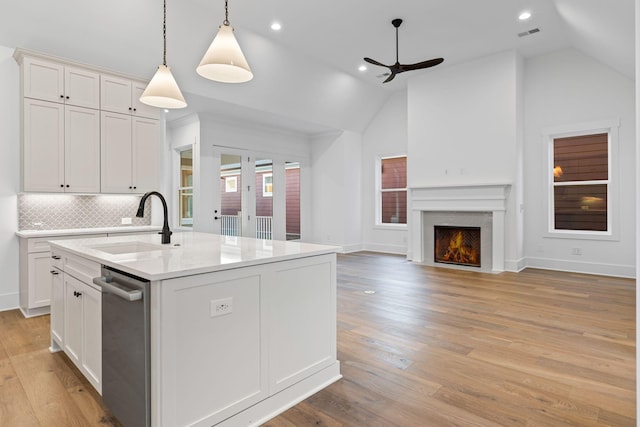 kitchen with lofted ceiling, decorative light fixtures, an island with sink, and white cabinets