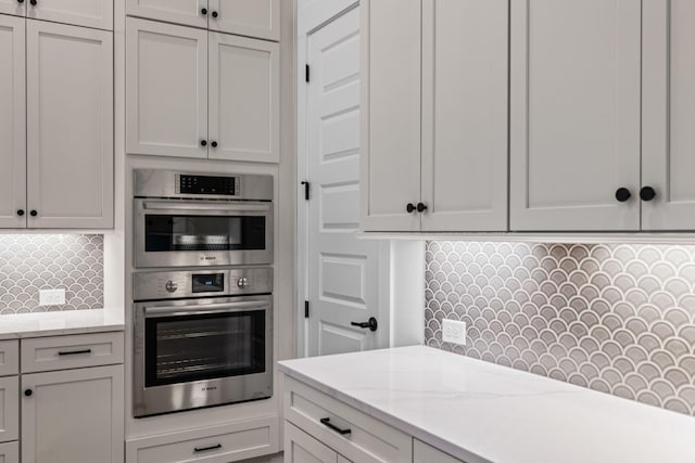 kitchen featuring tasteful backsplash, light stone counters, white cabinets, and double oven