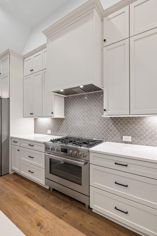 kitchen featuring white cabinets, decorative backsplash, light hardwood / wood-style floors, stainless steel appliances, and custom range hood