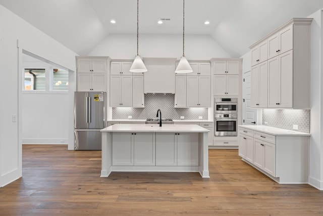 kitchen with lofted ceiling, decorative light fixtures, stainless steel appliances, and a center island with sink