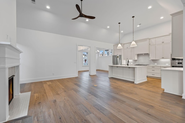 kitchen featuring tasteful backsplash, appliances with stainless steel finishes, an island with sink, pendant lighting, and ceiling fan