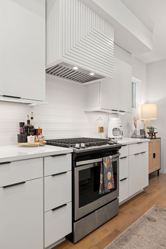 kitchen with white cabinets, light hardwood / wood-style floors, wall chimney exhaust hood, and gas range