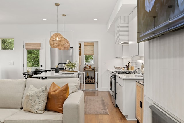 kitchen featuring stainless steel appliances, light hardwood / wood-style floors, hanging light fixtures, and white cabinets