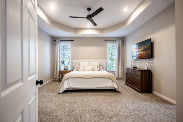 carpeted bedroom with ceiling fan, a tray ceiling, and multiple windows