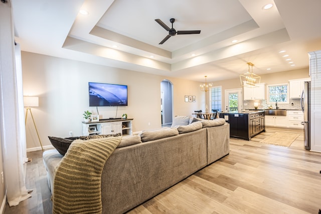 living room featuring a tray ceiling, sink, light hardwood / wood-style floors, and ceiling fan with notable chandelier