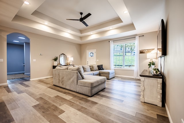 living room with ceiling fan, a raised ceiling, and light wood-type flooring