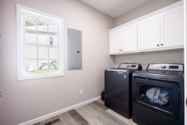 laundry area with electric panel, cabinets, washing machine and dryer, and light wood-type flooring