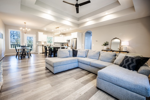 living room with a tray ceiling, ceiling fan with notable chandelier, and light wood-type flooring