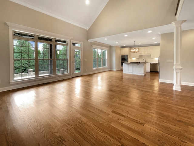 unfurnished living room with high vaulted ceiling, light wood-type flooring, decorative columns, and plenty of natural light