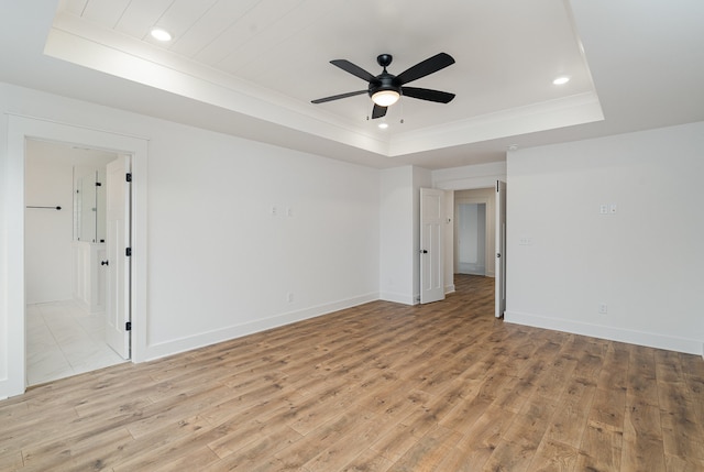 empty room featuring ceiling fan, light wood-type flooring, and a tray ceiling