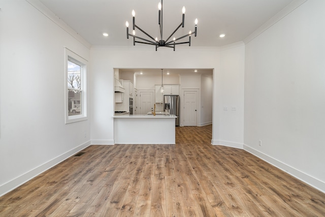 unfurnished living room featuring light wood-type flooring, a chandelier, and crown molding