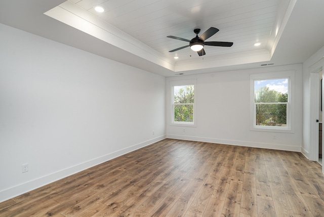 empty room featuring a tray ceiling, hardwood / wood-style floors, ceiling fan, and plenty of natural light