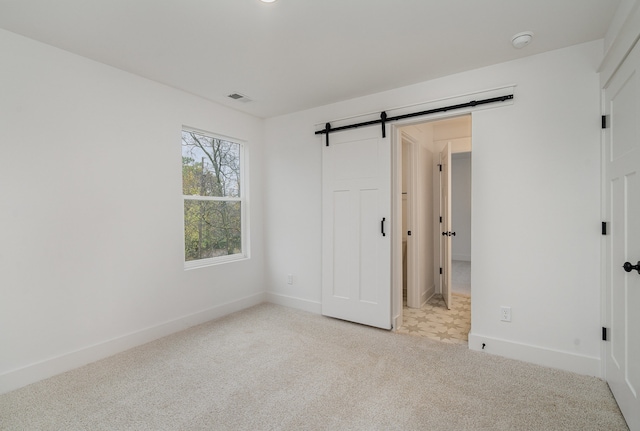 unfurnished bedroom featuring a barn door and light colored carpet