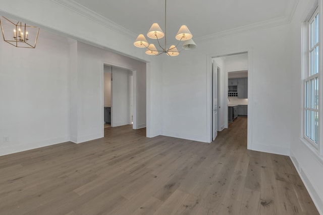 unfurnished dining area with light wood-type flooring, a healthy amount of sunlight, crown molding, and an inviting chandelier