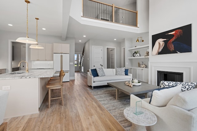 living room featuring a high ceiling, sink, light hardwood / wood-style flooring, built in shelves, and beam ceiling