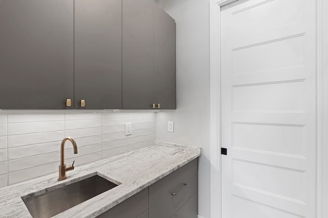 kitchen featuring decorative backsplash, gray cabinets, light stone counters, and sink