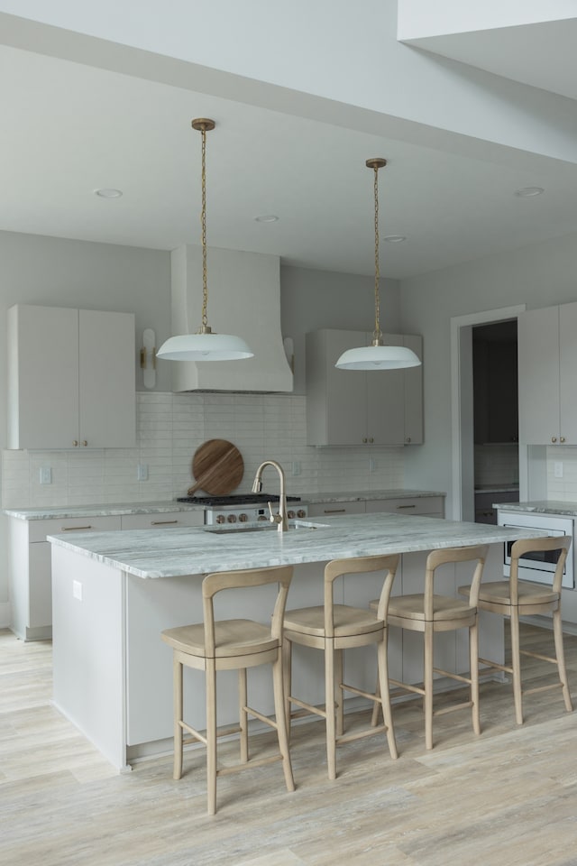 kitchen with backsplash, gray cabinets, light hardwood / wood-style flooring, and a spacious island