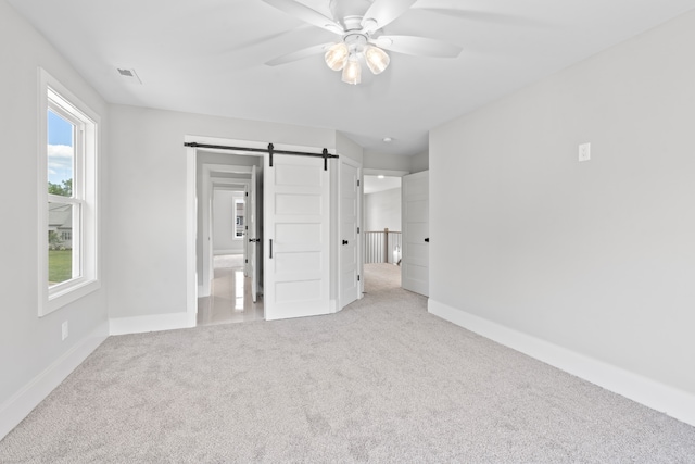 unfurnished bedroom featuring a barn door, ensuite bathroom, ceiling fan, and light colored carpet