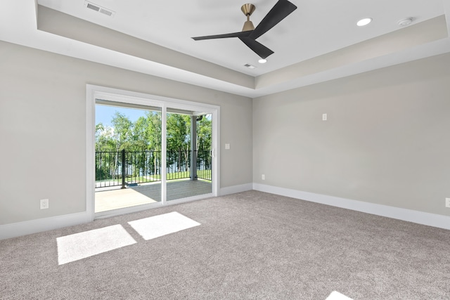 carpeted spare room with a tray ceiling and ceiling fan