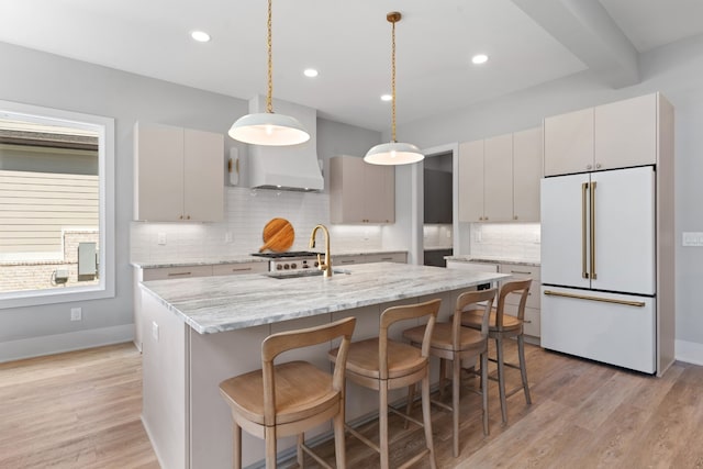 kitchen with a center island with sink, sink, high end white fridge, decorative light fixtures, and light hardwood / wood-style floors