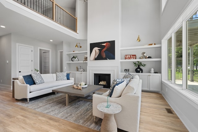 living room with built in shelves, light hardwood / wood-style floors, and a high ceiling