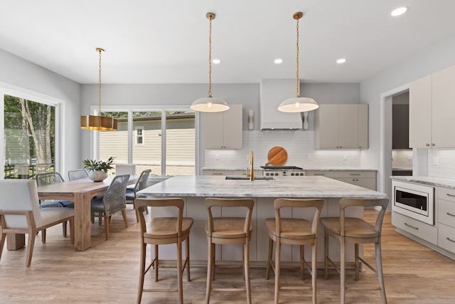 kitchen with a kitchen island with sink, sink, appliances with stainless steel finishes, tasteful backsplash, and custom range hood