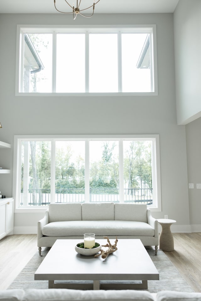 living room with built in features, a towering ceiling, light hardwood / wood-style floors, and an inviting chandelier