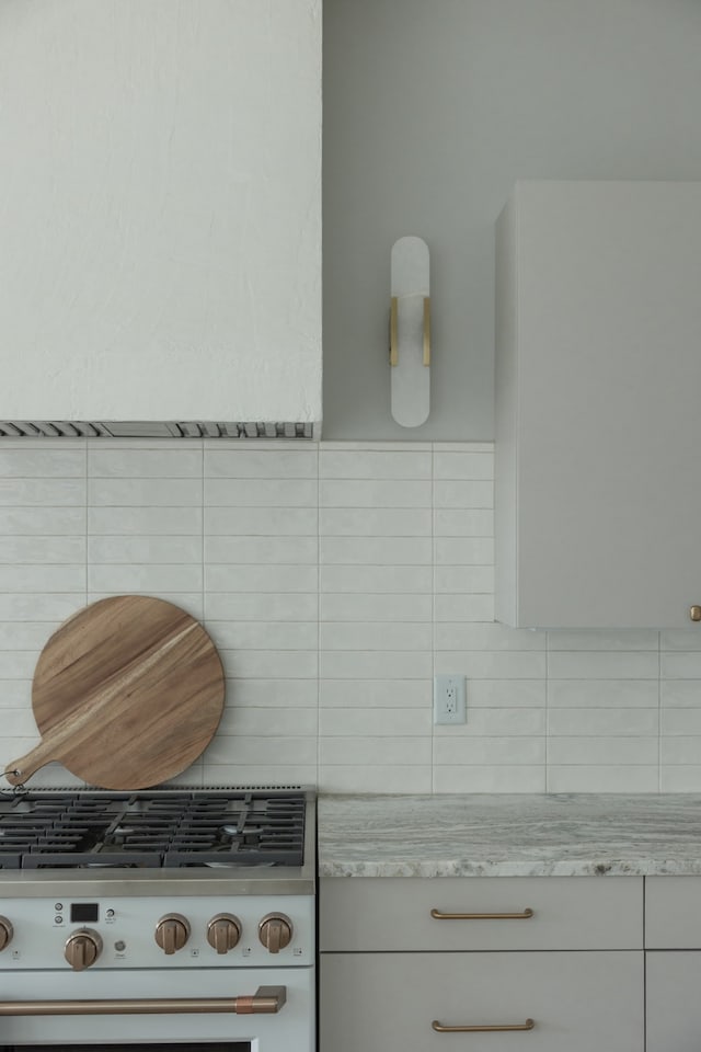 details featuring light stone countertops, range, tasteful backsplash, and white cabinetry