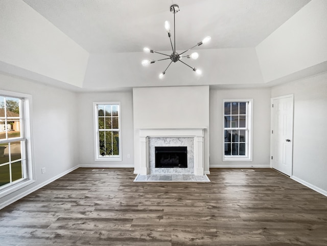 unfurnished living room featuring dark wood-type flooring, a chandelier, a premium fireplace, and a raised ceiling