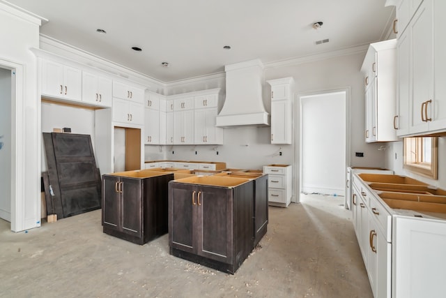 kitchen with a kitchen island, crown molding, white cabinetry, and premium range hood