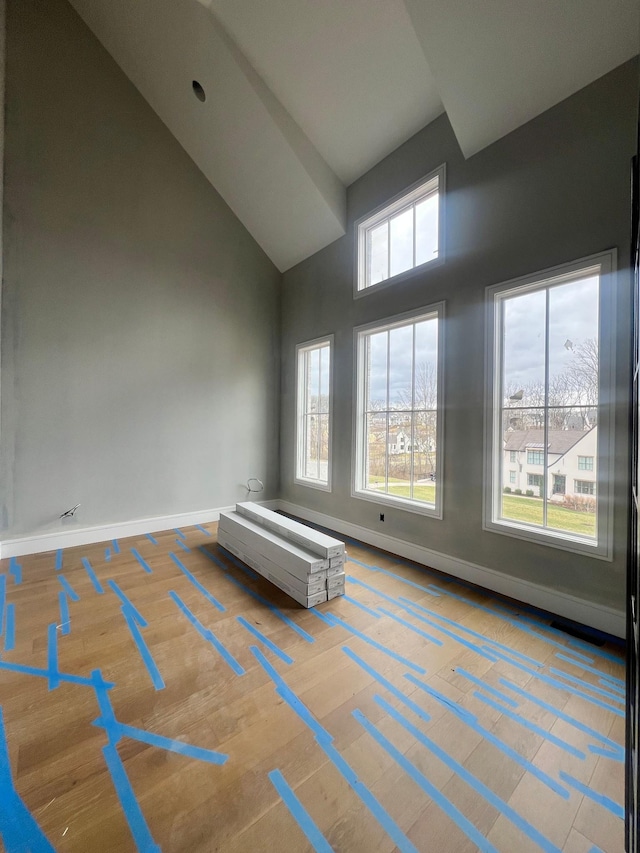 empty room featuring high vaulted ceiling, wood finished floors, and baseboards