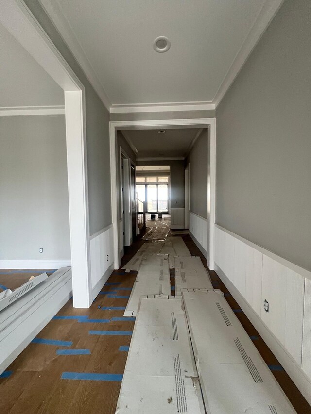 hall with a wainscoted wall, ornamental molding, and dark wood finished floors