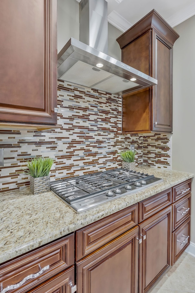 kitchen with light stone counters, tasteful backsplash, ornamental molding, wall chimney exhaust hood, and stainless steel gas stovetop