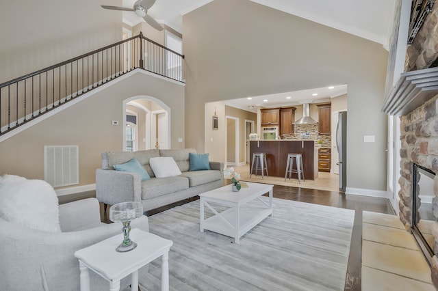 living room with light hardwood / wood-style floors, ornamental molding, ceiling fan, a fireplace, and a high ceiling