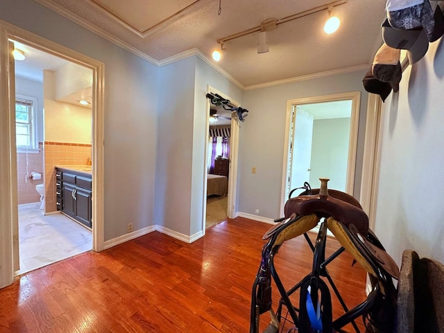 hallway with hardwood / wood-style floors, track lighting, tile walls, and ornamental molding