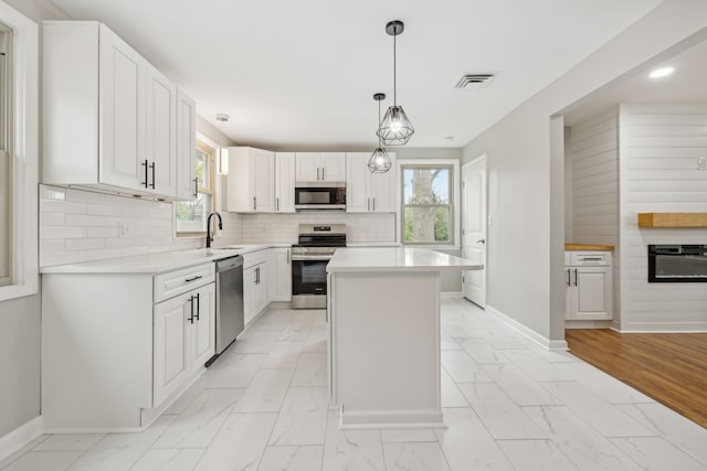 kitchen featuring stainless steel appliances, pendant lighting, a center island, decorative backsplash, and white cabinetry