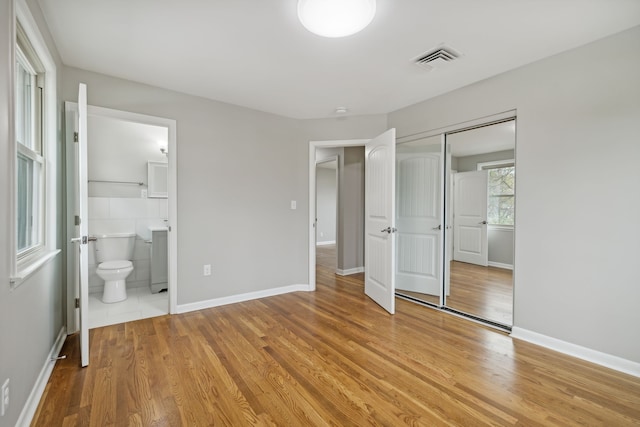 unfurnished bedroom featuring ensuite bathroom, light hardwood / wood-style floors, and a closet