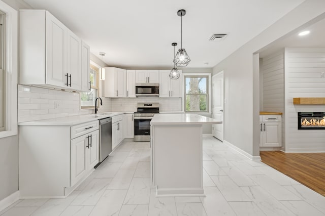 kitchen featuring white cabinetry, appliances with stainless steel finishes, pendant lighting, decorative backsplash, and a center island