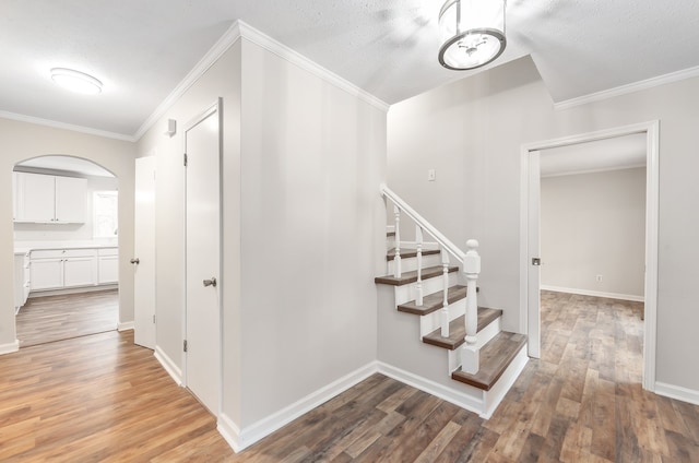 stairs with hardwood / wood-style floors, ornamental molding, and a textured ceiling