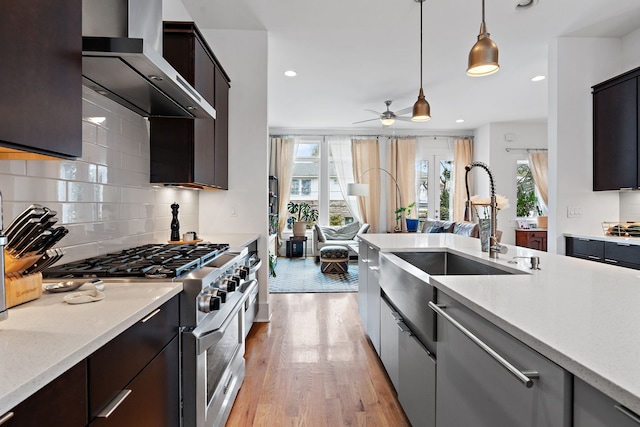 kitchen featuring light hardwood / wood-style floors, stainless steel stove, wall chimney range hood, backsplash, and pendant lighting