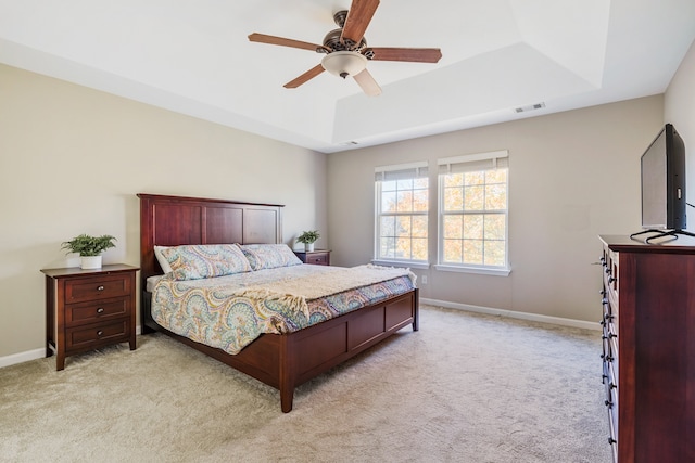 bedroom featuring light carpet, ceiling fan, and a tray ceiling