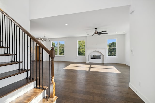 unfurnished living room with ceiling fan with notable chandelier and dark hardwood / wood-style flooring