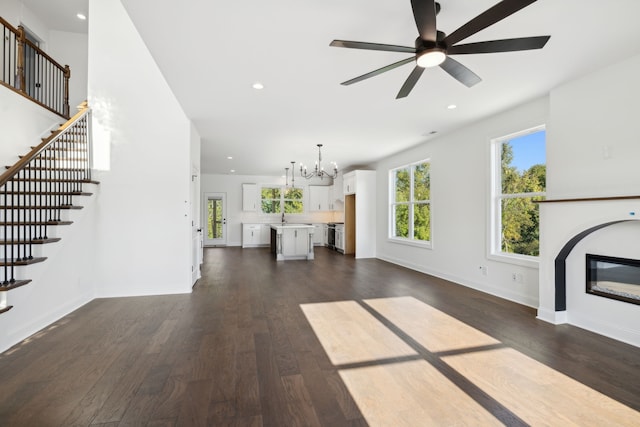 unfurnished living room with ceiling fan with notable chandelier and dark hardwood / wood-style flooring