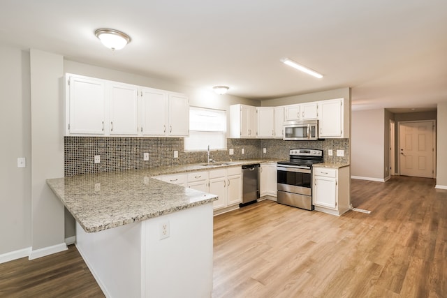 kitchen with light hardwood / wood-style floors, white cabinetry, sink, kitchen peninsula, and appliances with stainless steel finishes