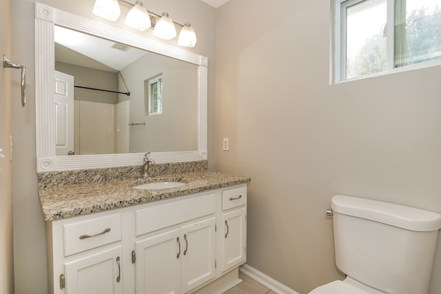 bathroom with walk in shower, a wealth of natural light, vanity, and toilet