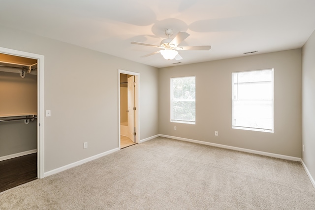 unfurnished bedroom featuring ensuite bath, light colored carpet, ceiling fan, a closet, and a walk in closet