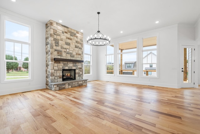 unfurnished living room with ornamental molding, light wood-type flooring, a notable chandelier, and a stone fireplace