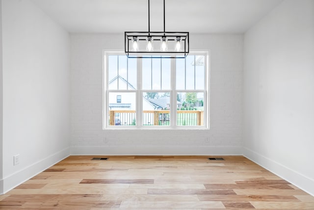 unfurnished dining area featuring light hardwood / wood-style floors, a notable chandelier, and brick wall