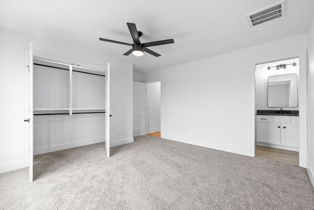 unfurnished bedroom featuring sink, ceiling fan, light colored carpet, connected bathroom, and a closet